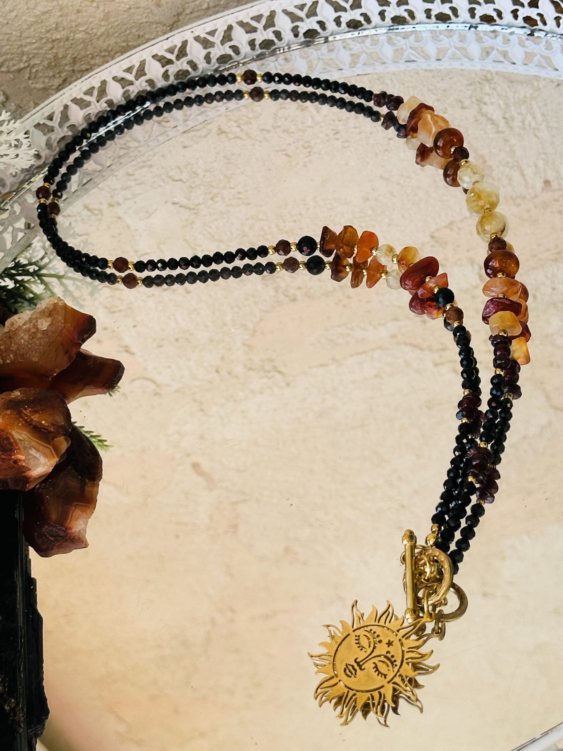 Naszyjnik „Jantar” z karneolem, granatem, cytrynem i turmalinem na złotej stali nierdzewnej z symbolem Słońca, ułożony na tle do prezentacji biżuterii.